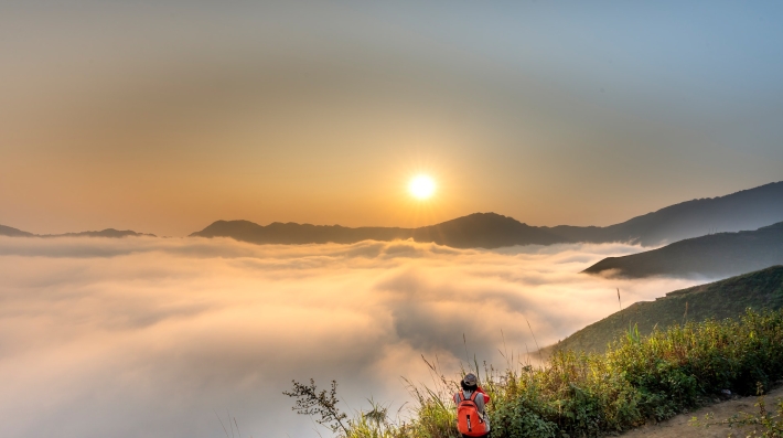 Um caminhante e um cachorro em uma trilha com vista para as nuvens.