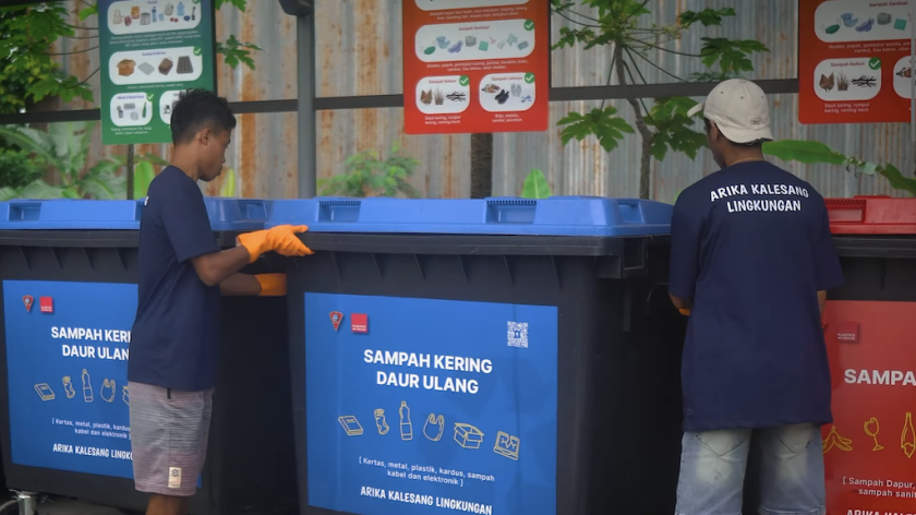 Two men placing a coloured bin in a waste collection facility. 